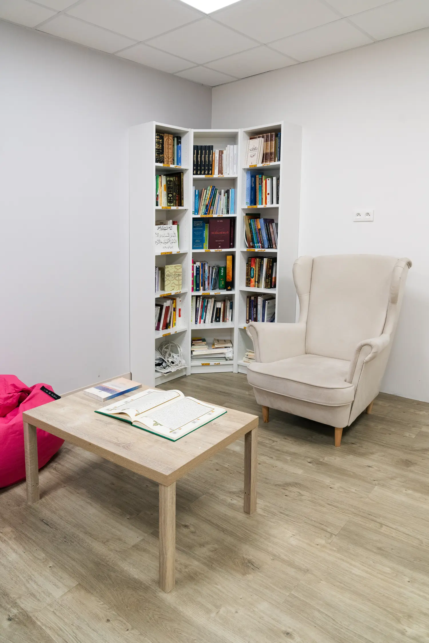 Les rayonnages de la bibliothèque, du sol au plafond, et au premier plan un Coran ouvert sur la table basse.