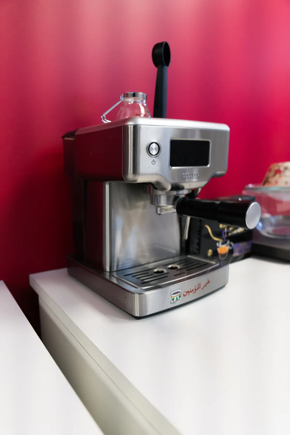 La machine à expresso sur le plan de travail, contre le mur cramoisi.