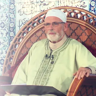 Chaykh ʿAbd Allāh Penot, assis, un livre ouvert devant lui.